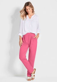 Witte blouse met knopen en opgerolde mouwen, gecombineerd met felroze elastische broeken en bruine sandalen, wat zorgt voor een casual outfit.