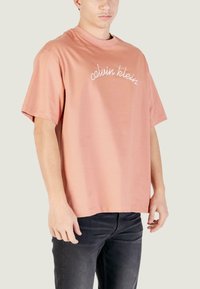 T-shirt oversize a maniche corte in tessuto di cotone rosa polvere con logo "calvin klein" ricamato bianco sul davanti.