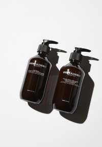 Två mörka bärnstensfärgade glasflaskor med svarta pumpdispenser. Etiketterna har vit text som anger handtvål och antibakteriell handkräm.