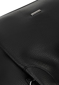 Zwarte leren tas met een gestructureerd oppervlak, zilveren merkje en een cirkelvormige hardware-accent. Voorzien van een klepsluiting en een slank ontwerp.