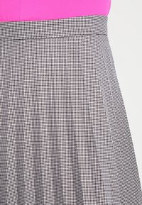 Sukně s černobílým vzorem ve stylu houndstooth, sklady, se hladkým pasem a texturovaným materiálem, prezentována na růžovém pozadí.