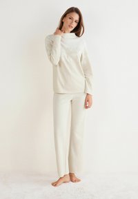 Crème-kleurige lounge-outfit met een getextureerde top met een subtiel patroon en bijpassende wijde broekspijpen. Zacht materiaal, ontspannen pasvorm.