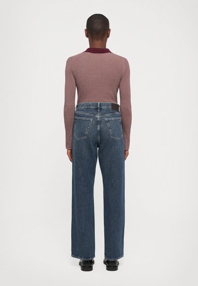 Langermet ribbestrikket genser i lys mauve med burgunder krage, kombinert med høyhårede blå denimjeans med baklommer.