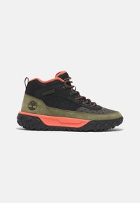 Chaussure de randonnée montante avec tige en mesh noir, daim vert olive, doublure orange, semelle intermédiaire épaisse orange et semelle extérieure noire robuste.