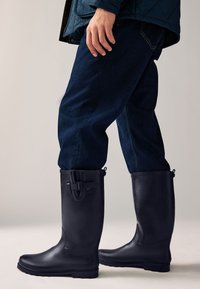 Sorte gummi-knæstøvler med mat finish, spænde detalje øverst og tekstureret sål, kombineret med mørke denimbukser.