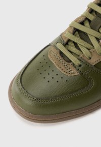 Sneaker verde em couro, com ponta arredondada, parte superior texturizada, atacadores a condizer e sola em borracha com detalhes subtis e perfurações.