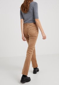 Braune Cord-Hosen mit geradem Bein, mit Gesäßtaschen und einer strukturierten Oberfläche, kombiniert mit einem grauen enganliegenden Oberteil und schwarzen Schuhen.