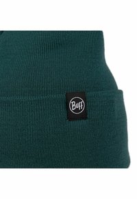Gorro de punto en verde oscuro, con una superficie texturizada y una etiqueta negra con el logo blanco de "Buff" en el puño.