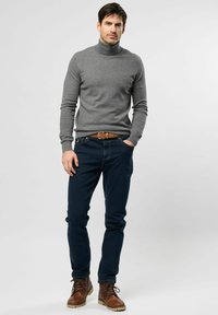 Un pull col roulé gris, un jean bleu foncé et des bottes marron à lacets. Le pull a une coupe ajustée, le jean est slim, accompagné d'une ceinture beige.