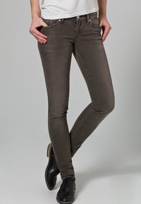 Jeans ajustados marrones de mezcla de algodón, con bolsillos frontales, detalles de costura sutiles y textura utilizada. Combinados con zapatos negros.