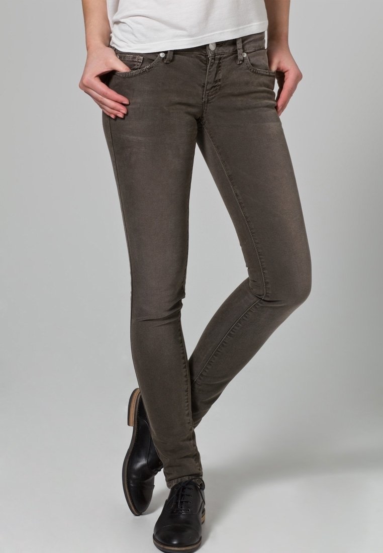 Jeans ajustados marrones de mezcla de algodón, con bolsillos frontales, detalles de costura sutiles y textura utilizada. Combinados con zapatos negros.