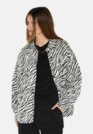 Jacke im Zebramuster in Schwarz und Weiß, oversized Design, aus strukturiertem Stoff, mit zwei Vordertaschen und Knopfverschluss.