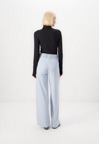 Un col roulé noir à manches longues associé à un pantalon large bleu clair avec une taille élastique, vu de dos.
