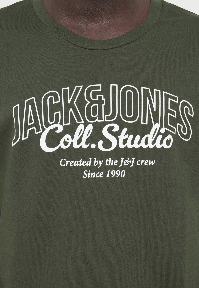 T-shirt vert olive en coton doux avec un texte imprimé blanc : "JACK & JONES Coll. Studio" et "Créé par l'équipe J&J depuis 1990."