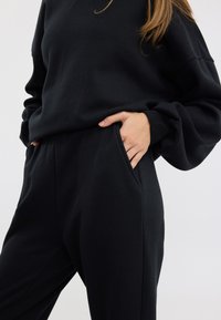 Svart träningsoutfit bestående av en sweatshirt med rund hals och avslappnade byxor. Båda plaggen har fickor och en mjuk, strukturerad yta.