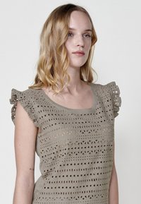 Vestido de manga corta en tono topo claro, con intrincados patrones de corte y mangas acampanadas con detalles rizados.