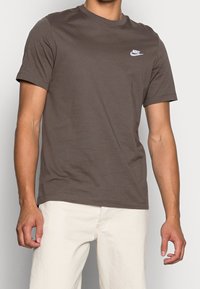 Brun bomullströja med kort ärm och rund hals. Har en vit Nike-logotyp på bröstet. Rak fåll.