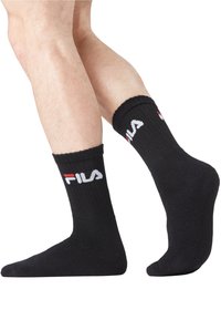 Chaussettes de sport noires à texture côtelée, avec un logo "FILA" blanc et rouge sur le revers, offrant un ajustement confortable autour de la cheville.