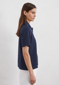 Navyblaue Polo-Shirt mit kurzen Ärmeln, einem klassischen Kragen und einer einheitlichen Textur. Hat eine lockere Passform und dezente Knopfdetails am Kragen.