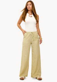 Lichtgroene en crèmekleurige gestreepte wijde broek met een elastische tailleband en trekkoord. Gelijkend met een aansluitend wit tanktop en sandalen.