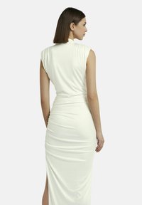 Abito bianco senza maniche con una silhouette aderente e una texture arricciata. Presenta uno spacco laterale e un tessuto liscio e elasticizzato.