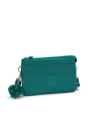 Prostokątna torebka na ramię w kolorze morskim z przednią kieszenią na zamek, naszywką z logo Kipling oraz przymocowanym pluszowym breloczkiem w kształcie małpki na białym tle.