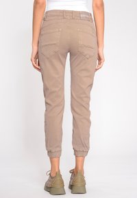 Pantalones cargo de color marrón claro con puños acanalados y múltiples bolsillos, que presentan un brillo sutil y una etiqueta de la marca en la cintura trasera.