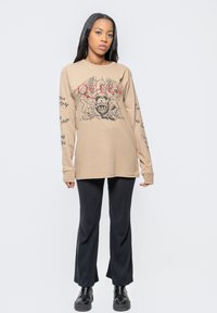 Beige long-sleeve t-shirt featuring a graphic print of a crowned skull and "QUEEN" text, paired with black flared pants and black boots.