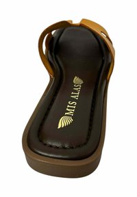 Sandalía marrón con parte superior de piel suave, suela marrón y detalle del logo dorado. Presenta un diseño minimalista y estilo de punta abierta.