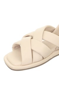 Beige Sandale mit überkreuztem Riemendesign, aus glattem Material gefertigt. Flacher Absatz mit dicker Kante. Weiches, gepolstertes Fußbett.