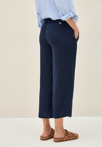 Marinblå, texturerade byxor med vida ben och fickor, med midjeband och ankellång design. Bruna sandaler med vita prickar.
