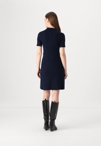 Abito a coste blu navy con maniche corte, vita aderente e gonna svasata. Indossato con stivali di pelle nera al ginocchio con cerniere.