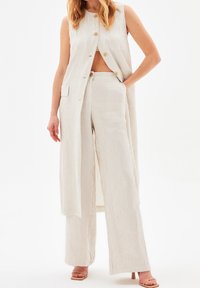 Sleeveless striped vest in beige with gold buttons, paired with wide-leg striped trousers. Smooth fabric with a relaxed fit and side pockets.