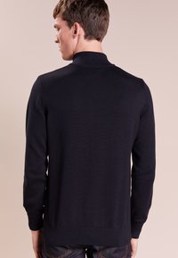 Schwarzer Strickpullover mit hohem Kragen und langen Ärmeln, mit einem gerippten Saum und Bündchen. Einfaches Design mit glatter Textur.