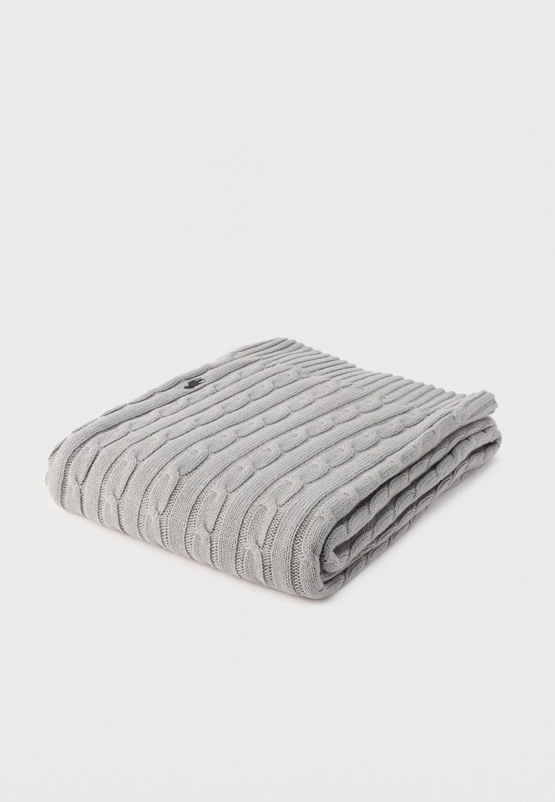 Ανοιχτό γκρι πλεκτό μάλλινο κασκόλ διπλωμένο, με ένα μικρό μαύρο κεντημένο λογότυπο σε μία γωνία, τοποθετημένο σε λευκό φόντο.