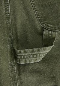Tejido verde oliva con un acabado texturizado, con un bolsillo visible y costuras reforzadas. El diseño tiene un estilo casual y utilitario.