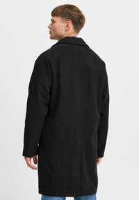 Svart ullblandingsfrakk med lang skjæring, bred krage og rett silhuett. Glatt tekstur og minimal detaljering på ryggen.