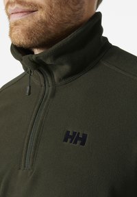Sudadera de forro polar verde con media cremallera, cuello alto y logotipo azul marino. Presenta un acabado texturizado y detalles de cremallera duradera.