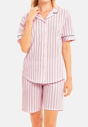 Kvinde iført lyserød og hvid vertikalt striped kortærmet knap-op skjorte og matchende knælange shorts-natdragter, stående med en hånd nær kraven.