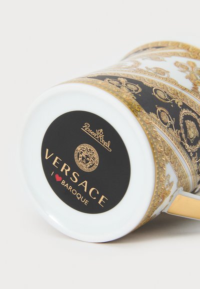 Porcelænskrus med sort og guld barokdesign. Har en glat hvid overflade, et forgyldt håndtag og en sort cirkulær mærkat med brand på bunden.