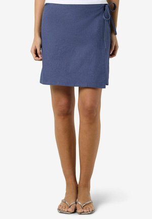 Blå midilengde omslagsnederdel bundet i siden, båret med hvid top og mønstrede flip-flop sandaler.