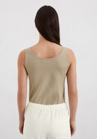 Beige ärmelloses Shirt mit rundem Ausschnitt, aus weichem Stoff, kombiniert mit hellen, elastischen Hosen mit Gummibund. Minimalistisches Design.