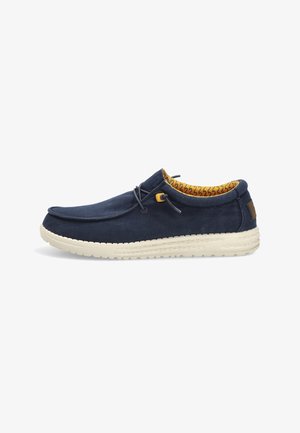 Zapato casual azul marino sin cordones, con suela beige, cordones elásticos ajustables y forro interior amarillo con estampado.