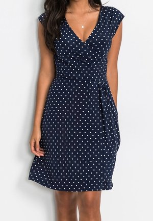 Robe bleu marine à pois blancs, manches courtes style cape, encolure en V et design portefeuille. Tissu lisse avec une coupe fluide à la taille.