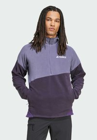 Terrex fleece pullover har et farveblokdesign i lys og mørk lilla, lynlås i nakken, lange ærmer og en blød tekstur. Justerbar kantdetalje.