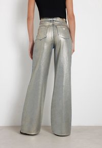 Metaliczne srebrne dżinsy o szerokich nogawkach z teksturowanym wykończeniem, z tylnymi kieszeniami i przeszywanym dołem. W połączeniu z dopasowaną czarną bluzką.