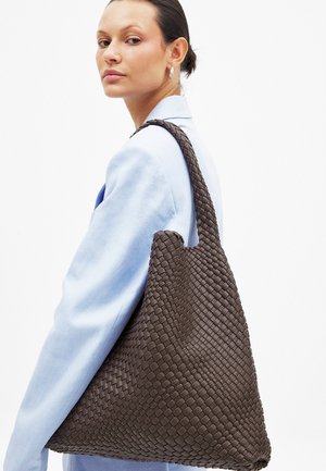 Vævet brun læder tote bag med en rummelig, vinklet form og en enkelt skulderrem, præsenteret på en neutral baggrund.