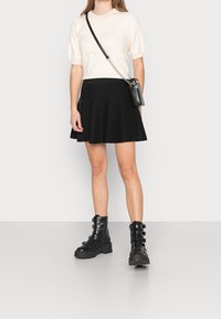 Krämskjutande stickad tröja, svart utsvängd kjol och svarta snörkängor med spännen; modellen bär en liten svart axelväska.