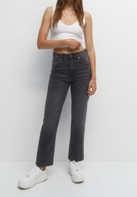Jeans de denim gris de cintura alta con un diseño de pierna recta, que cuentan con bolsillos frontales y detalles de costura sutiles, llevados con zapatillas blancas.