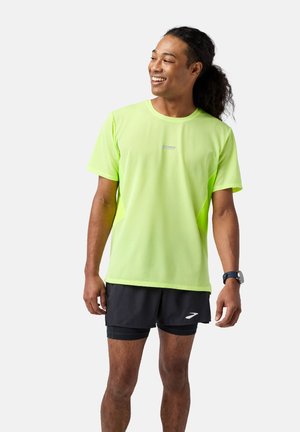 Neon grøn, T-shirt med korte ærmer til sport med et struktureret mønster, parret med sorte shorts med et hvidt logo. Velegnet til sportsaktiviteter.